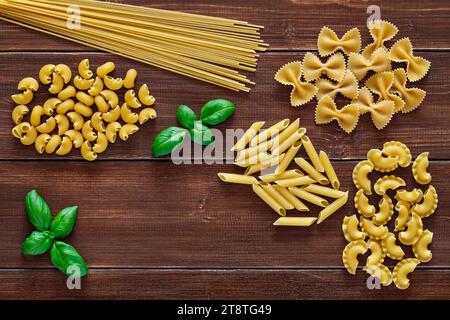 Spaghetti, farfalle, pipe rigatoni, maccheroni, penne rigate, cresta di gallo, raw, leaf of basil, on wooden brown planks dark background, top view, s Stock Photo