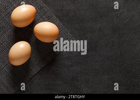 Eggs whole chicken, three pieces, on dark background, top view, space to copy text. Stock Photo