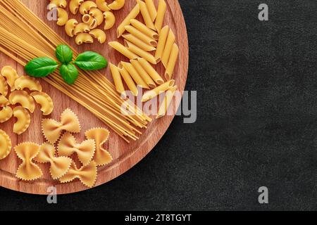 Spaghetti, farfalle, rigatoni, maccheroni, penne rigate, cresta di gallo, raw, basil, on wooden brown plank tabletop background, top view, space to co Stock Photo