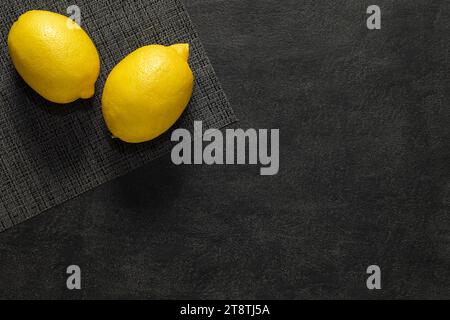 Lemons, two whole on a gray tablecloth, on dark background, top view, space to copy text. Stock Photo