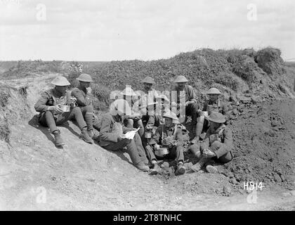 A New Zealand soldier reading from a German magazine, World War I, New Zealand soldiers eating a midday meal near the front line. One of the group translates from a German magazine found in a dugout. Photograph taken Grevillers 20 August 1918 Stock Photo