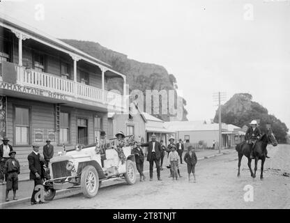 Whakatane township, Whakatane Hotel with rocky ciffs behind, photographed circa 1910s. Looks along a street with the Whakatane Hotel on the left. A touring car with a man and a woman as passengers in the back seat, with a group of people standing around, and a young man on horseback, watching from the middle of the road Stock Photo