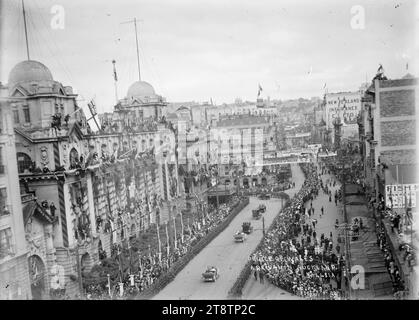 Queen Street, Auckland, New Zealand, during arrival of the Prince of Wales, View taken from a high vantage point looking up Queen Street, Auckland, New Zealand, during the arrival of the Prince of Wales, April 1920. The Post Office and surrounding buildings are decorated with flags and foliage. A motorcade of cars are driving up Queen Street and turning left into Custom Street; people are lining the streets watching the procession Stock Photo