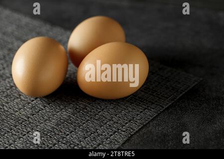 Three whole chicken eggs on dark surface, selective focus. Stock Photo