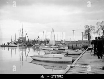 Shortland Wharf, Thames, Group of men, including two with cameras, standing on the wharf in the foreground on the right. Yachts, fishing boats and a dredge are tied up close by. A launch with four men on board, is approaching the wharf on the left. Yacht registration numbers include: TS12, TS73, TS29, TS50, TS35, TS41. in early 1900s Stock Photo
