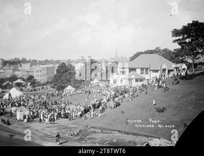 Crowd alongside Myers Kindergarten, Myers Park, Auckland, New Zealand, Crowd, including many children, alongside Myers Kindergarten and on the kindergarten balconies, Myers Park, Auckland, New Zealand, circa 1917. Some of the children are on playground equipment. The shops in upper Queen Street can be seen in the background on the lefthand side. Tents are erected on the grassy areas around the kindergarten Stock Photo