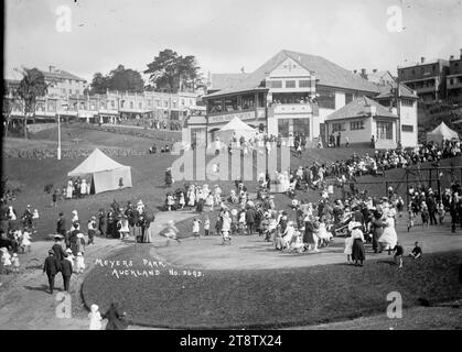 Crowd alongside Myers Kindergarten, Myers Park, Auckland, New Zealand, Crowd, including many children, alongside Myers Kindergarten and on the kindergarten balconies, Myers Park, Auckland, New Zealand, circa 1917. Some of the children are on playground equipment. The shops in upper Queen Street can be seen in the background. Tents are erected on the grassy areas around the kindergarten Stock Photo