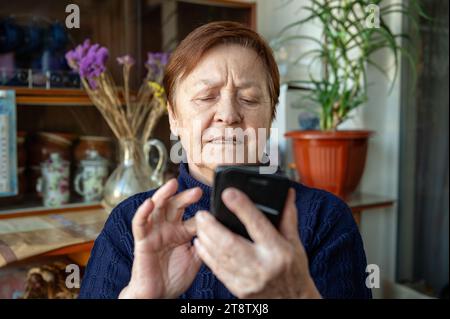 Portrait of an elderly woman using a smartphone. Elderly woman near window at home using mobile phone Stock Photo