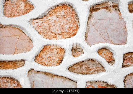 Wall from red and grey stones background, texture irregular shapes, stone fence with white putty. Stock Photo