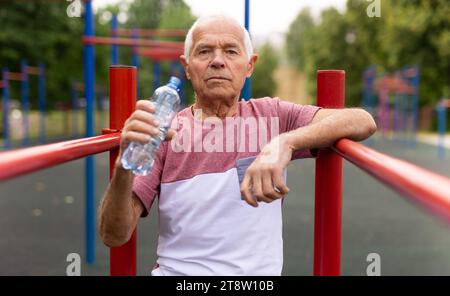 Elderly man drinks water after a workout on the playground Stock Photo