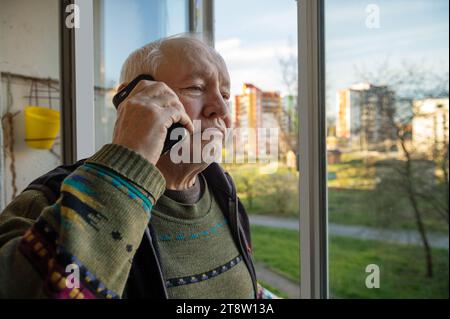 Portrait of an elderly man using a smartphone. Elderly man near the window at home using mobile phone Stock Photo