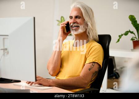 Male computer programmer talking on smart phone while using computer Stock Photo