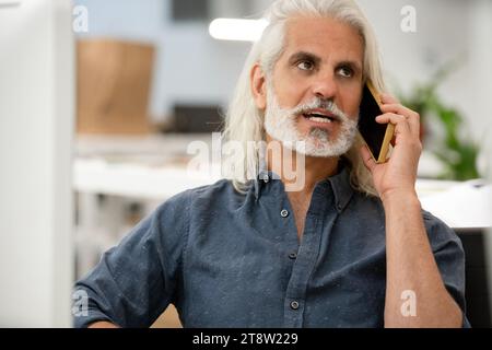 Free lance designer talking on smart phone while working on computer Stock Photo