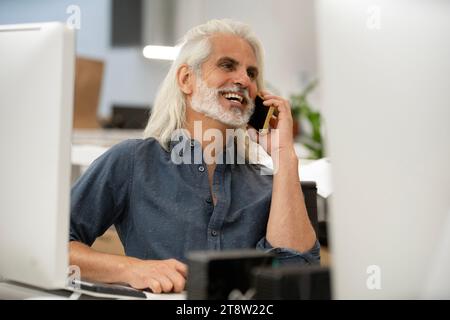 Free lance designer talking on smart phone while working on computer Stock Photo