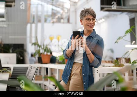 Female entrepreneur using smart phone while standing indoors Stock Photo