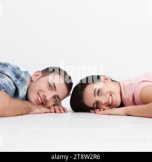 Happy young couple, lying on the floor, look at each other and dream of furniture for new apartment. Mock up for design. Stock Photo