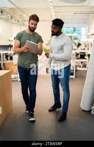 Two coworkers standing while discussing over digital tablet Stock Photo