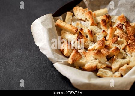 Crackers, dried baked pieces of white bread on craft paper on dark background, selective focus. Stock Photo
