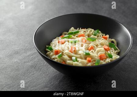 Noodles instant cooked with vegetables carrot and green onion dark bowl, selective focus. Stock Photo