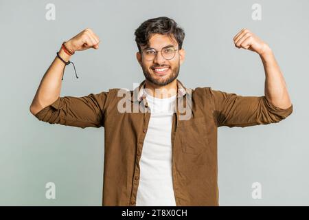I am strong and independent. Young Indian man showing biceps and looking confident, feeling power strength to fight for rights, energy to gain success win. Guy isolated on gray studio background Stock Photo