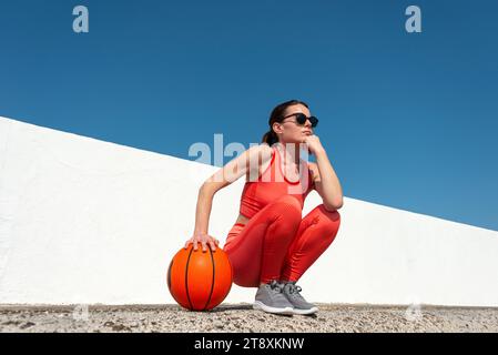 Female basketball player, crouching holding a basketball, outside in the sun. Stock Photo