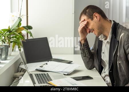 Frustrated overworked caucasian businessman, entrepreneur, product manager, programmer, sits at a desk in the office, massaging the bridge of his nose Stock Photo