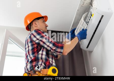 Repairman using a screwdriver fixing modern air conditioner, Male technician cleaning air conditioner indoors, Maintenance and repairing concepts Stock Photo