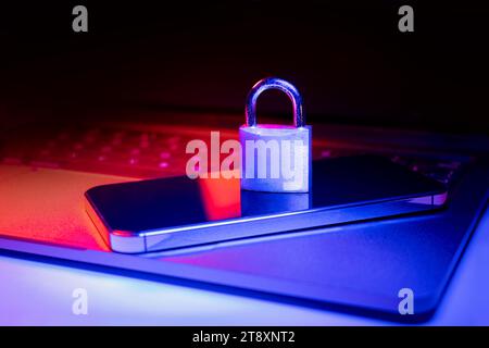 Closeup of a padlock on a laptop and phone illuminated with blue and red light.Phishing, cybersecurity danger or ransomware attack. Encrypted privacy Stock Photo