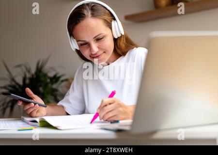 Young woman student doing paper homework at home using workbook and digital devices. Stock Photo