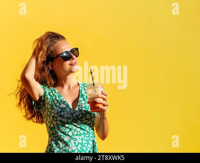 Beautiful brunette woman wearing green dress enjoying summer. Woman in front of yellow wall on street in city. Stock Photo