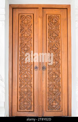 Wooden double-leaf carved door with beautiful ornaments and iron handles. Stock Photo