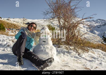 latin woman sitting on frozen ground next to snowman Stock Photo