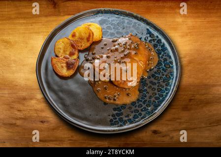 Green pepper beef tenderloin with baked potatoes in black plate on wooden table Stock Photo