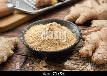 Bowl of ginger ground to powder and whole ginger roots on kitchen table.  A grater with grated ginger root in the background. Stock Photo
