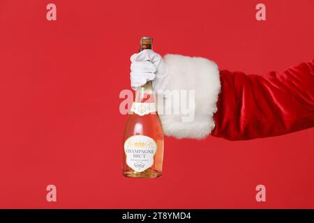 Santa Claus holding bottle of champagne on red background, closeup Stock Photo