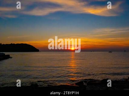 Beautiful sunset or sunrise with orange sun shining through clouds above the horizon and reflecting on the lake water. Stock Photo