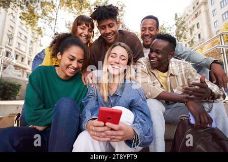 Diverse group university friends sitting on stairs in street city. Happy students using smartphones. Stock Photo