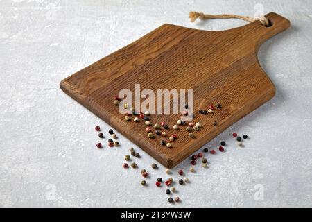 Brown wooden cutting board with scattered multi-colored peppercorns on a gray stone table Stock Photo