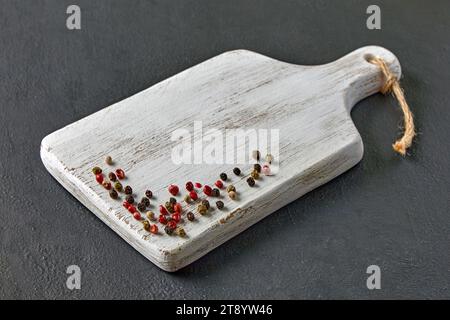 White wooden cutting board with scattered multi-colored peppercorns on a black stone table Stock Photo