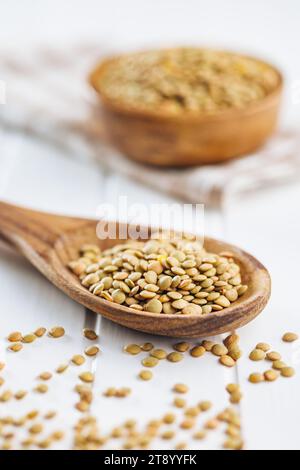 Uncooked lentil legumes in wooden spoon on the white table. Stock Photo