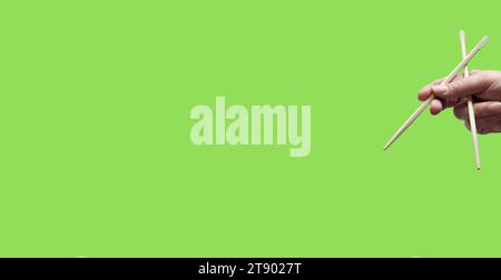 Asian chopsticks held in human hand on monochrome light green background. Without food. No identifiable person. Copy space Stock Photo