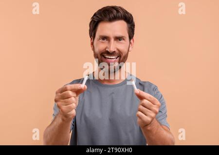 Stop smoking concept. Happy man holding pieces of broken cigarette on light brown background Stock Photo