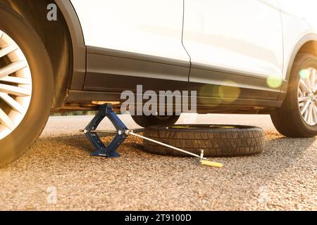 Car lifted by scissor jack and spare wheel on roadside Stock Photo