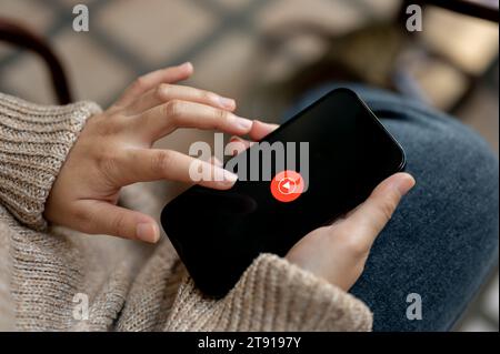 Chiang Mai, Thailand - Nov 21 2023: Close-up image of a woman using Youtube music application on her IPhone14 while sitting outdoors. Youtube music lo Stock Photo