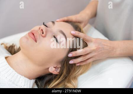 Healer performing by lightly touched set of 32 points of access bars on young woman head, stimulating positive change thoughts and emotions Stock Photo