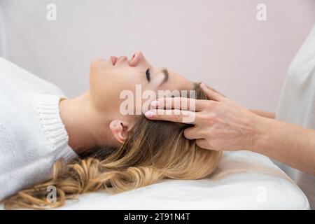 Healer performing by lightly touched set of 32 points of access bars on young woman head, stimulating positive change thoughts and emotions Stock Photo