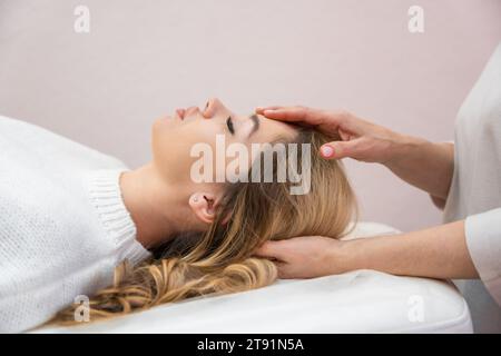 Healer performing set of 32 points of access bars on young woman head, stimulating positive change thoughts and emotions in salon. Alternative Stock Photo