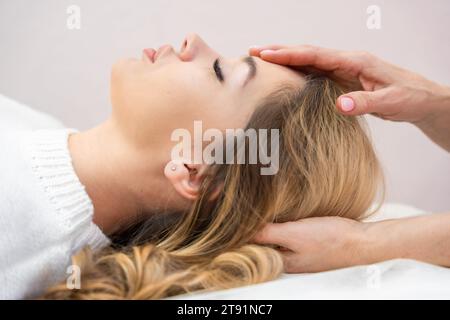 Healer performing set of 32 points of access bars on young woman head, stimulating positive change thoughts and emotions in salon. Alternative Stock Photo