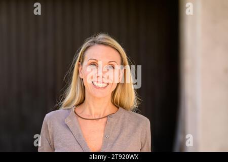 Portrait of an attractive blonde smiling woman, in front of wooden wall Stock Photo