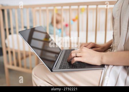 Side view closeup of young mother using laptop with focus on hands typing, work from home or internet research on baby care, copy space Stock Photo